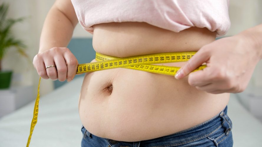 Closeup of obese woman measuring her big belly with yellow measuring tape. Concept of dieting