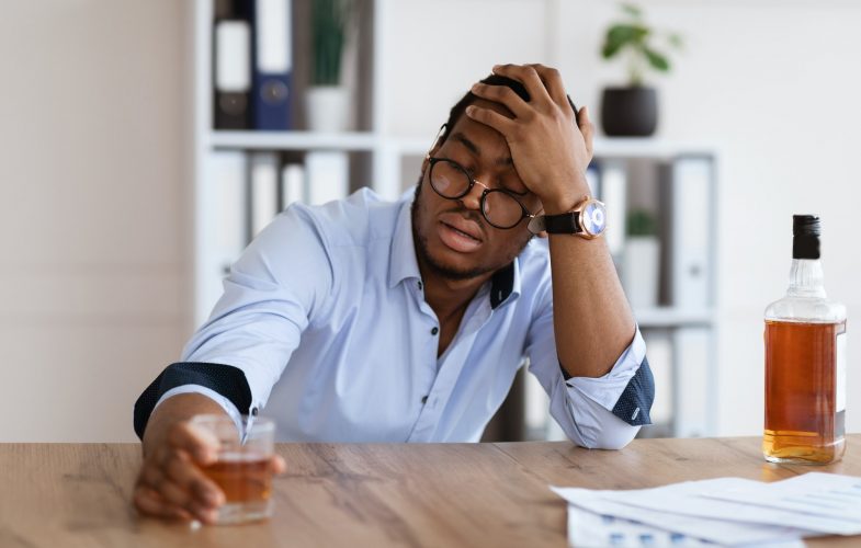 Drunk black manager sitting in his office and drinking