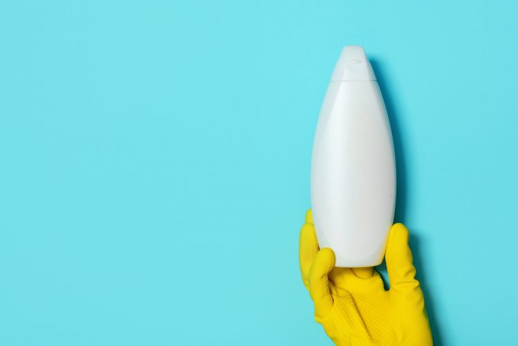 Hand hoding shampoo or soap bottles on blue background. Personal care products during coronavirus