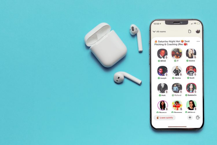 Open the Clubhouse app on your iPhone screen and have your wireless headphones on a blue background.