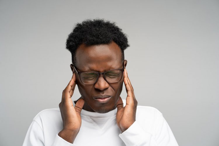 Overwhelmed black employee man in glasses suffering from loud sound, dizziness, headache, isolated.
