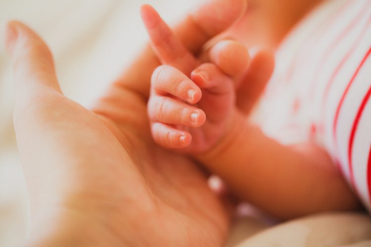 The index finger of a newborn baby in the mother's hand