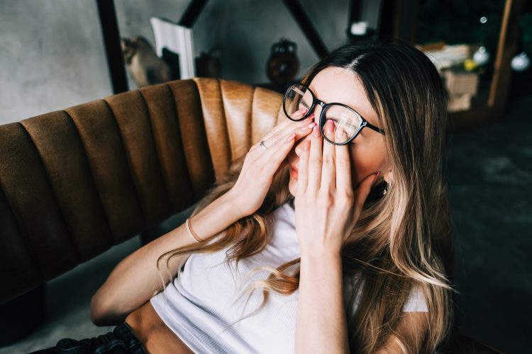 Young woman rubs her eyes after using glasses. Eye pain or fatigue concept.