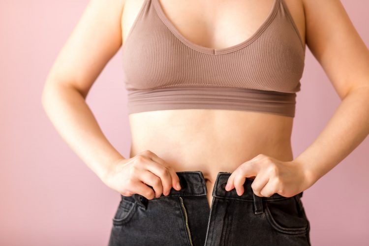 young woman trying to button up denim pants on fat waist