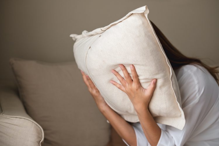 A depressed, stressed woman putting her face on a pillow, mental problem and health care concept