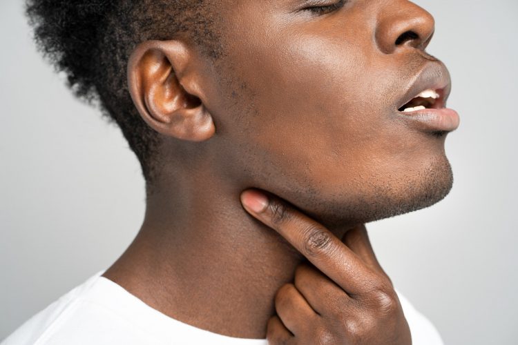 Black man touches fingers of sore throat, thyroid gland, isolated on studio gray background