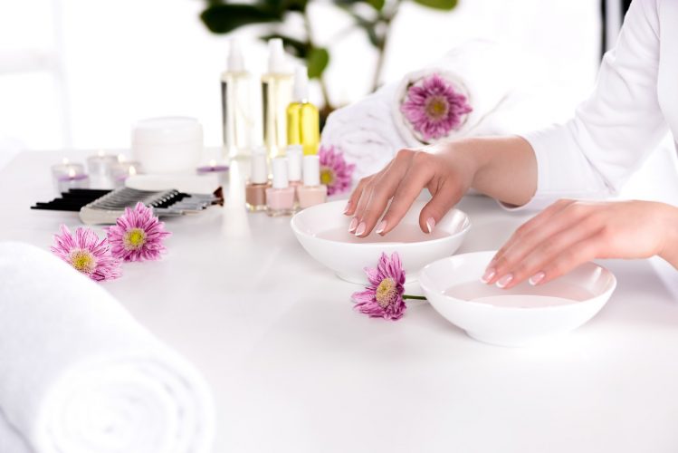 cropped image of woman receiving bath for nails at table with flowers, towels, candles, aroma oil