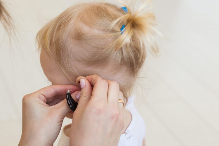 Hearing aid in baby girl's ear. Toddler child wearing a hearing aid at home. Disabled child