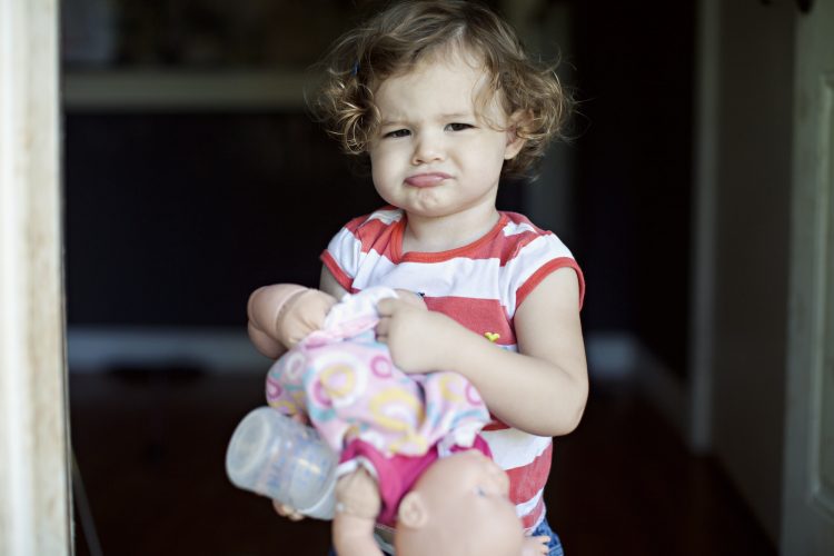 mad little toddler holding a doll