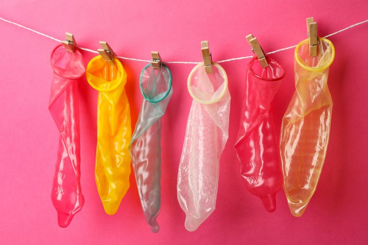 Multicolored condoms hanging on the rope on pink background