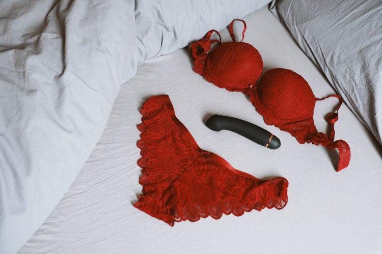 red lace bra and panties lingerie set with vibrator dildo on bed as female masturbation concept