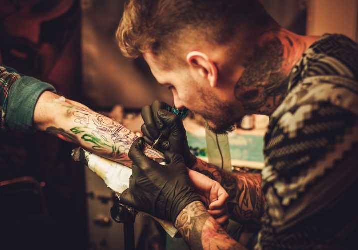 Tattoo artist makes a tattoo on a man's hand.