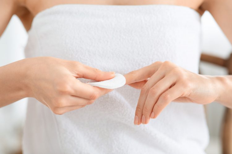 Woman removing lacquer from manicured nails with white cotton pad