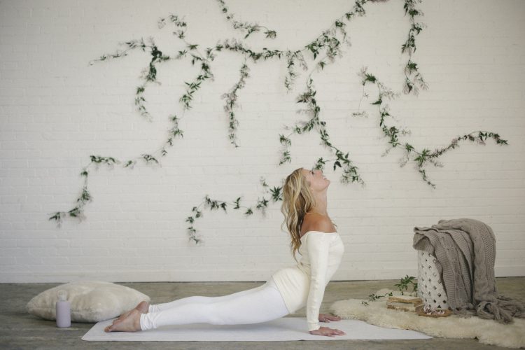 A woman lying on a yoga mat in a room, arching her back in a stretch.
