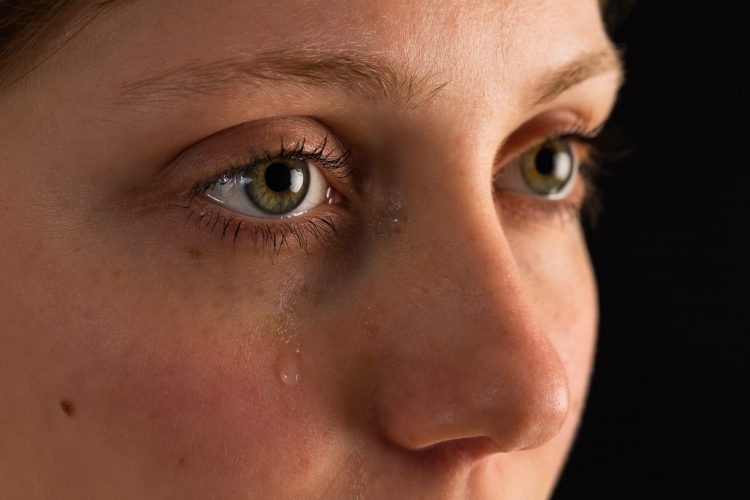 Face of unhappy female in tears from close up in darkness