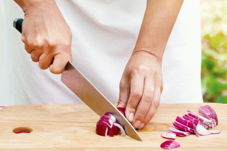 Female hands cut onions on wooden board