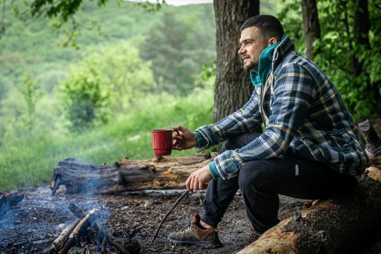 A man on a hike sits by the fire and warms himself.