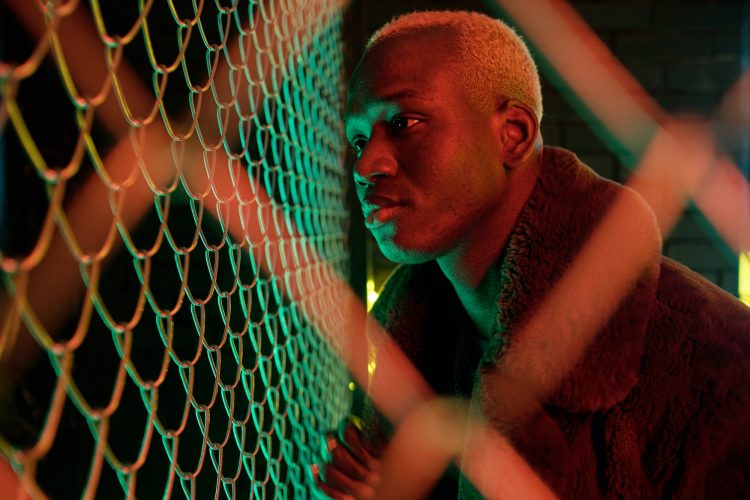 Young African man in furcoat standing close to bars
