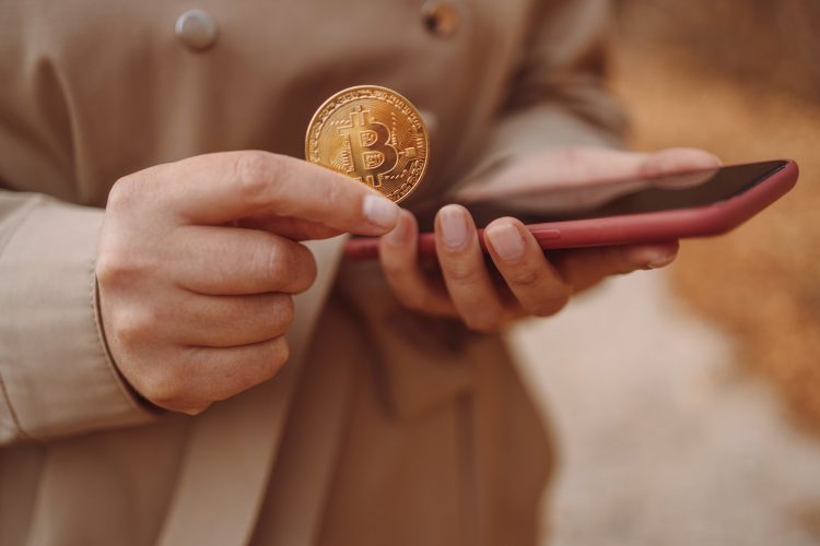 Golden bitcoin coin in a business woman. Trading bitcoin in a mobile application on a smartphone