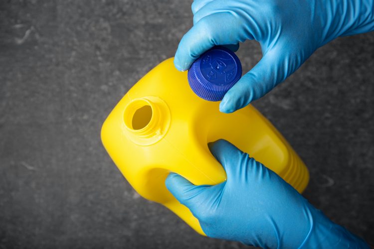 Human hand in protective glove holding a bleach bottle