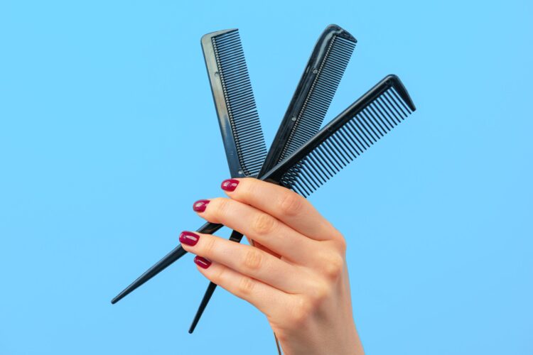 Female hand holding hair comb against blue background