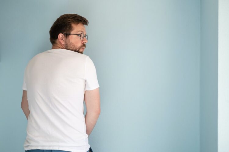 Shameless man urinating on the wall of the house or masturbates, looking around in fear and surprise