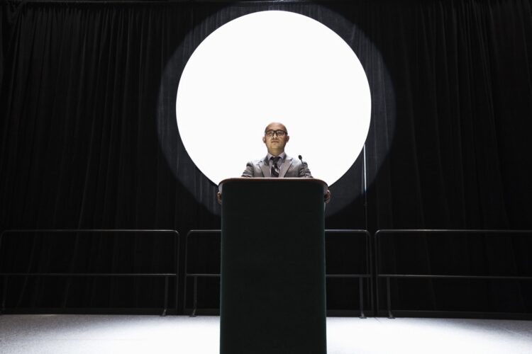 An asian businesman standing at a podium giving a talk at a convention.