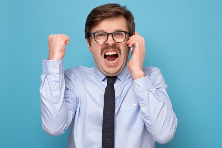 Pissed off angry mature guy with mustache in black glasses, shouting at smartphone and shaking fist