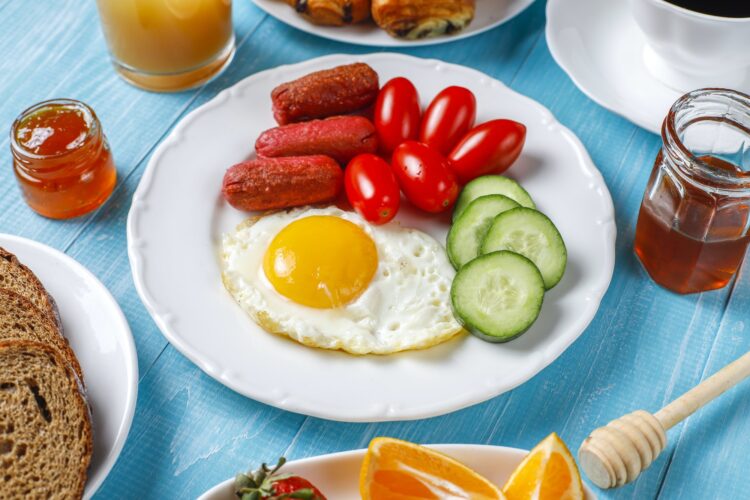 cocktail sausages,fried eggs,cherry tomatoes,sweets,fruits and a glass of peach juice.
