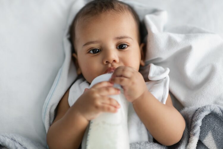 Cute little African American child drinking from baby bottle
