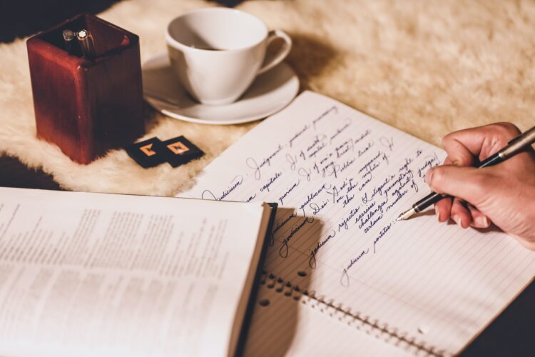A person writing with a fountain pen into a notebook on a desk.