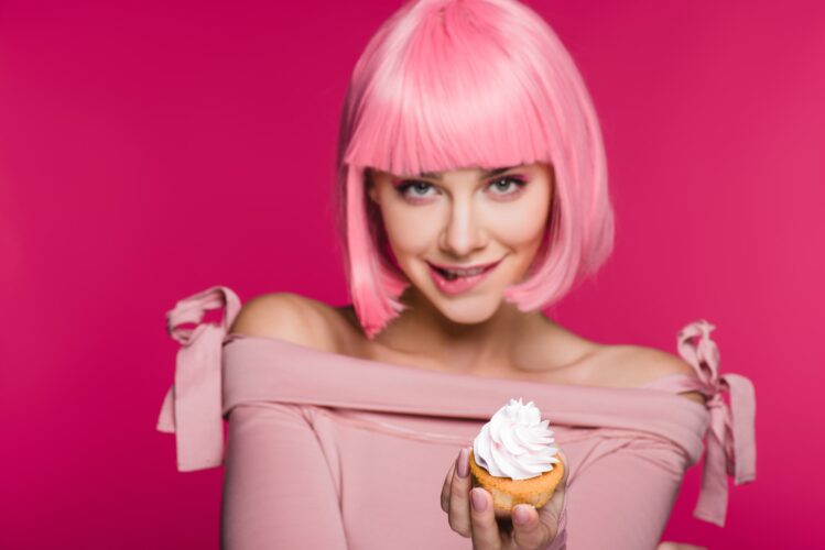 attractive sensual girl biting lip and holding cupcake isolated on pink