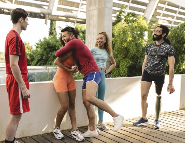 Multiracial group of athletes in a park. Asian friend hugs African american woman.