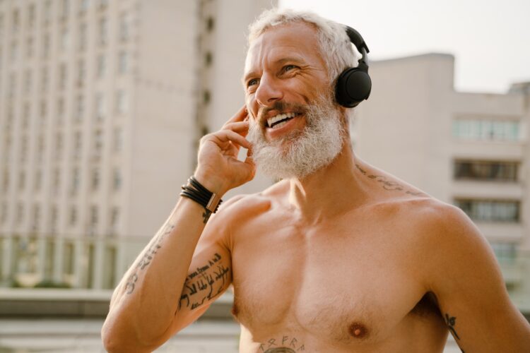 Shirtless mature man listening music with headphones outdoors