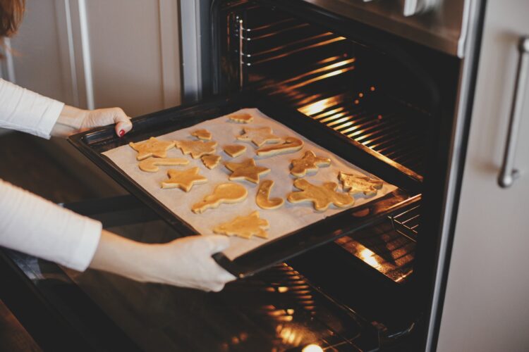 Woman putting tray with christmas cookies in oven in modern kitchen. Baking gingerbread cookies