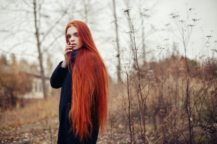 Woman with long red hair walks in autumn on the street. Mysterious dreamy look and the image of the