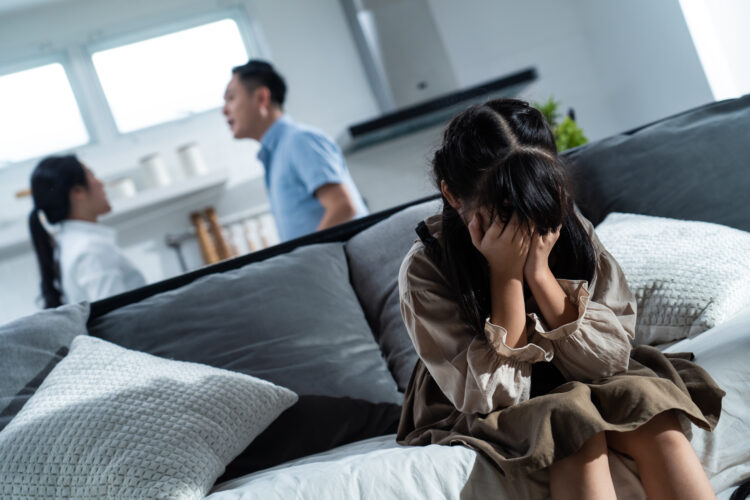 Asian girl kid sitting and crying while parents having fighting or quarrel conflict at home.