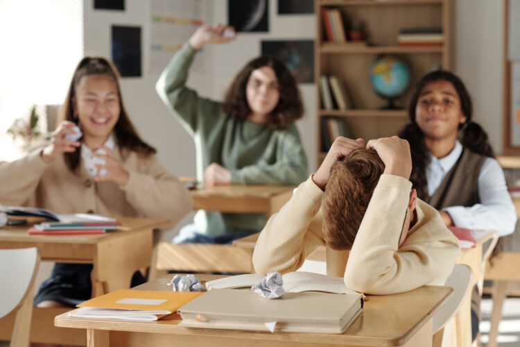 Discriminated schoolboy covering his head while defending from classmates