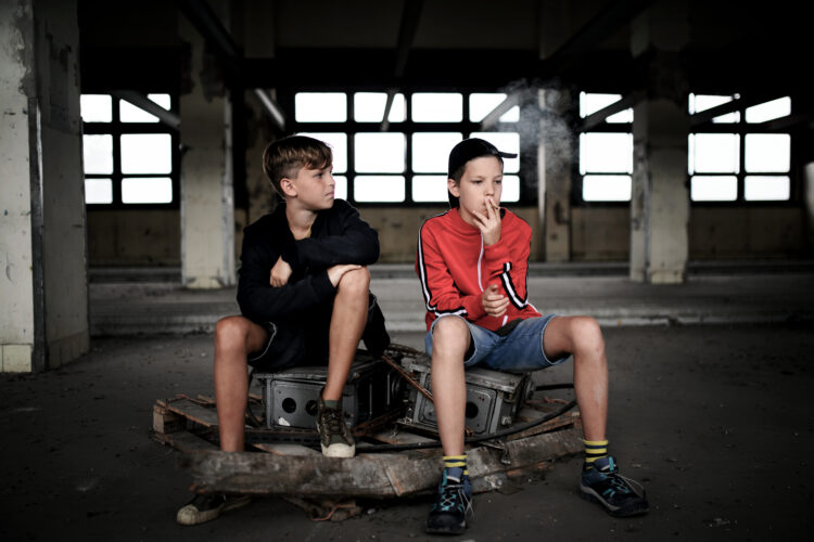 Group of teenagers boys indoors in abandoned building, smoking cigarettes.