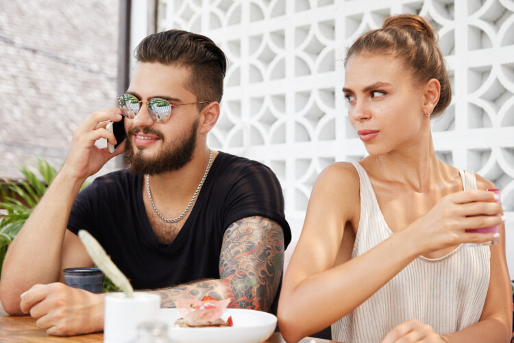 Irritated angry jealous young female being discontent as her bearded boyfriend speaks with unknown p