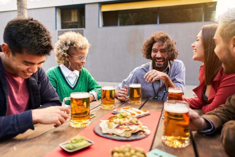 Multiracial friends having fun drinking beer together at terrace bar.