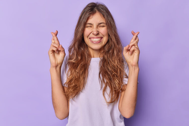 Optimistic young woman anticipates good news keeps fingers crossed begs for positive outcome wears c