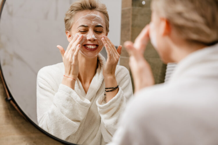 Attractive young woman applying moisturizer on her face