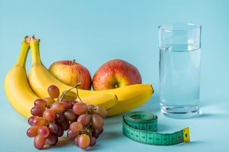 Fruit, glass of water and measuring tape on a blue background.