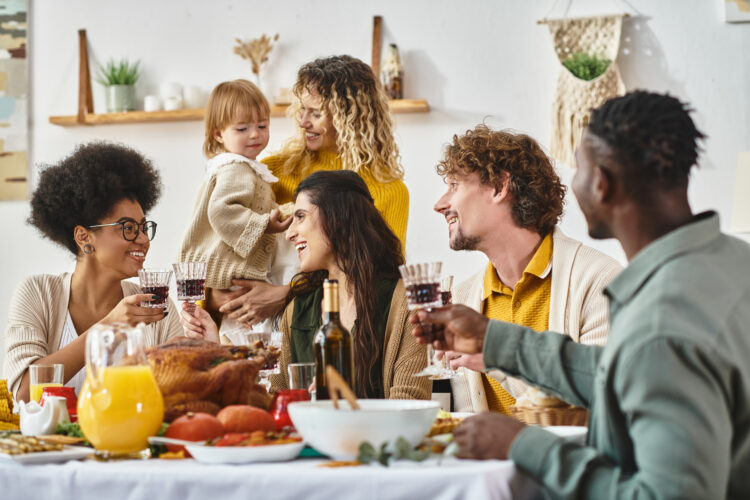 Happy Thanksgiving, cheerful multiethnic women clinking glasses of wine near friends and family