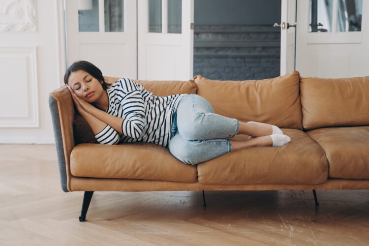 Overworked young woman is sleeping on leather couch at home. Daytime nap on sofa.