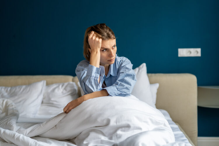 Stressed woman sit on bed with morning bad mood, touch head, suffer headache after night of insomnia