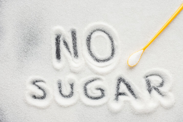 top view of"no sugar" lettering written on granulated sugar with plastic spoon