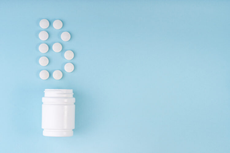 Vitamin B pills dropped from bottle on blue. Letter B inscription from tablets. Vitamin B12 concept.