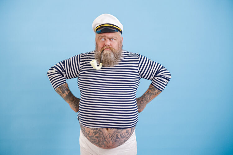 Funny bearded fat man in sailor suit with smoking pipe on light blue background